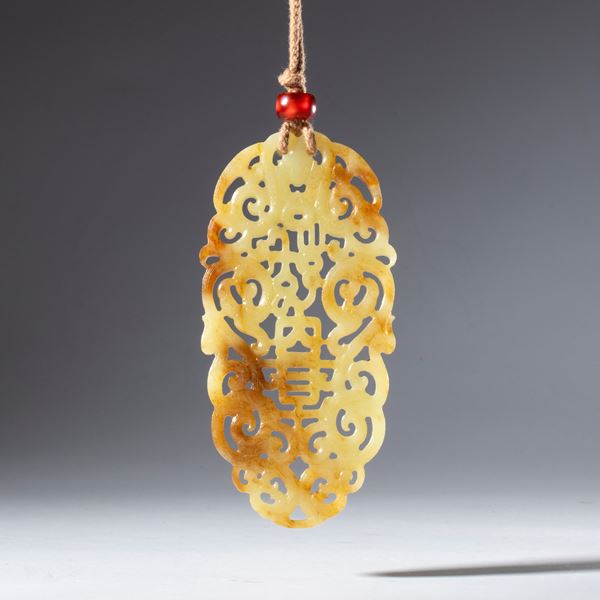 Ornamental pendant in perforated and engraved Hotan russet jade. Suspended from a cotton string held at the base by a carnelian bead. China, 18th century.