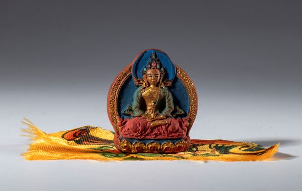 A small painted clay Tza Tza wrapped in a piece of silk fabric for daily Buddhist worship. Tibet or Nepal, 20th century.
