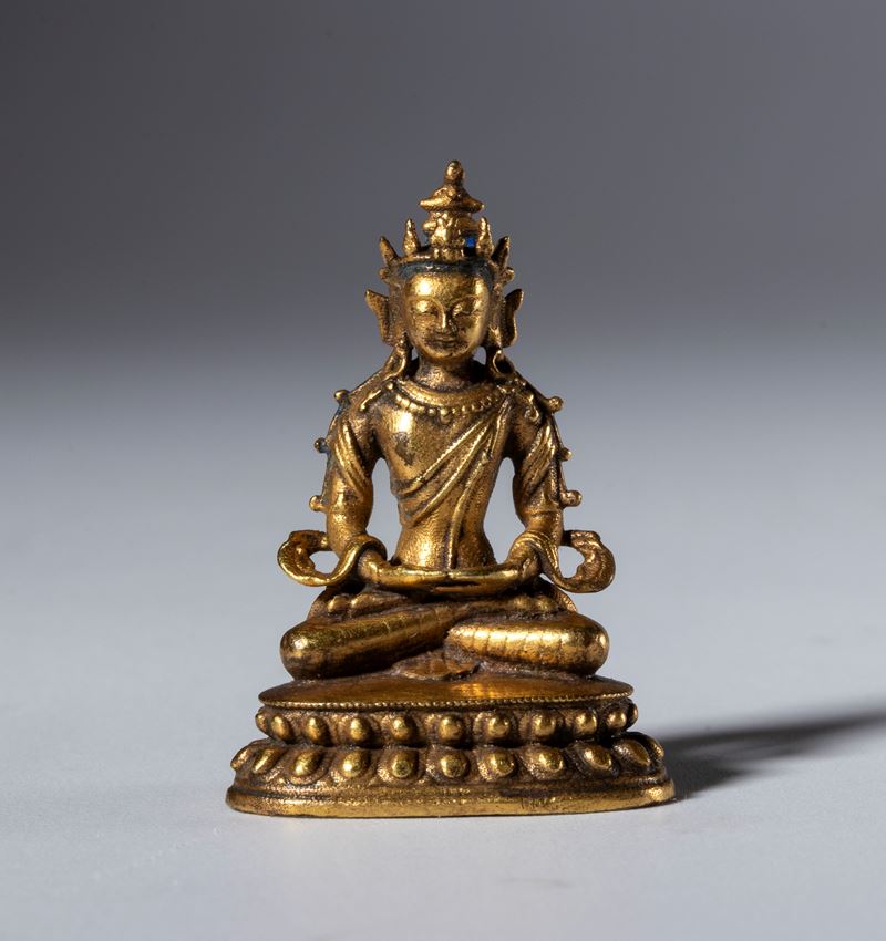 Piccola statua di Buddha in rame dorato con base cava per reliquie. Tibet, XIX secolo