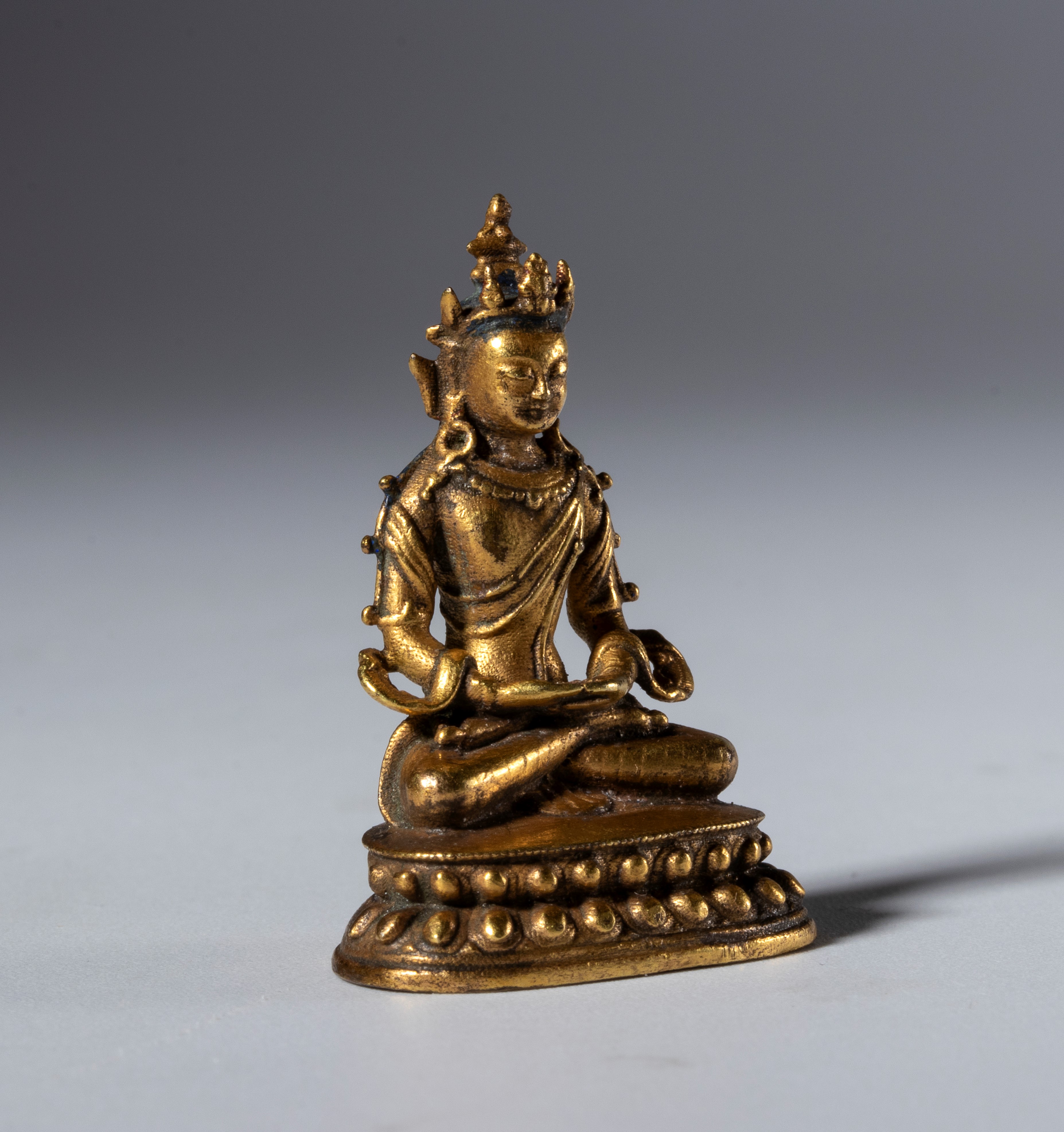Piccola statua di Buddha in rame dorato con base cava per reliquie. Tibet, XIX secolo