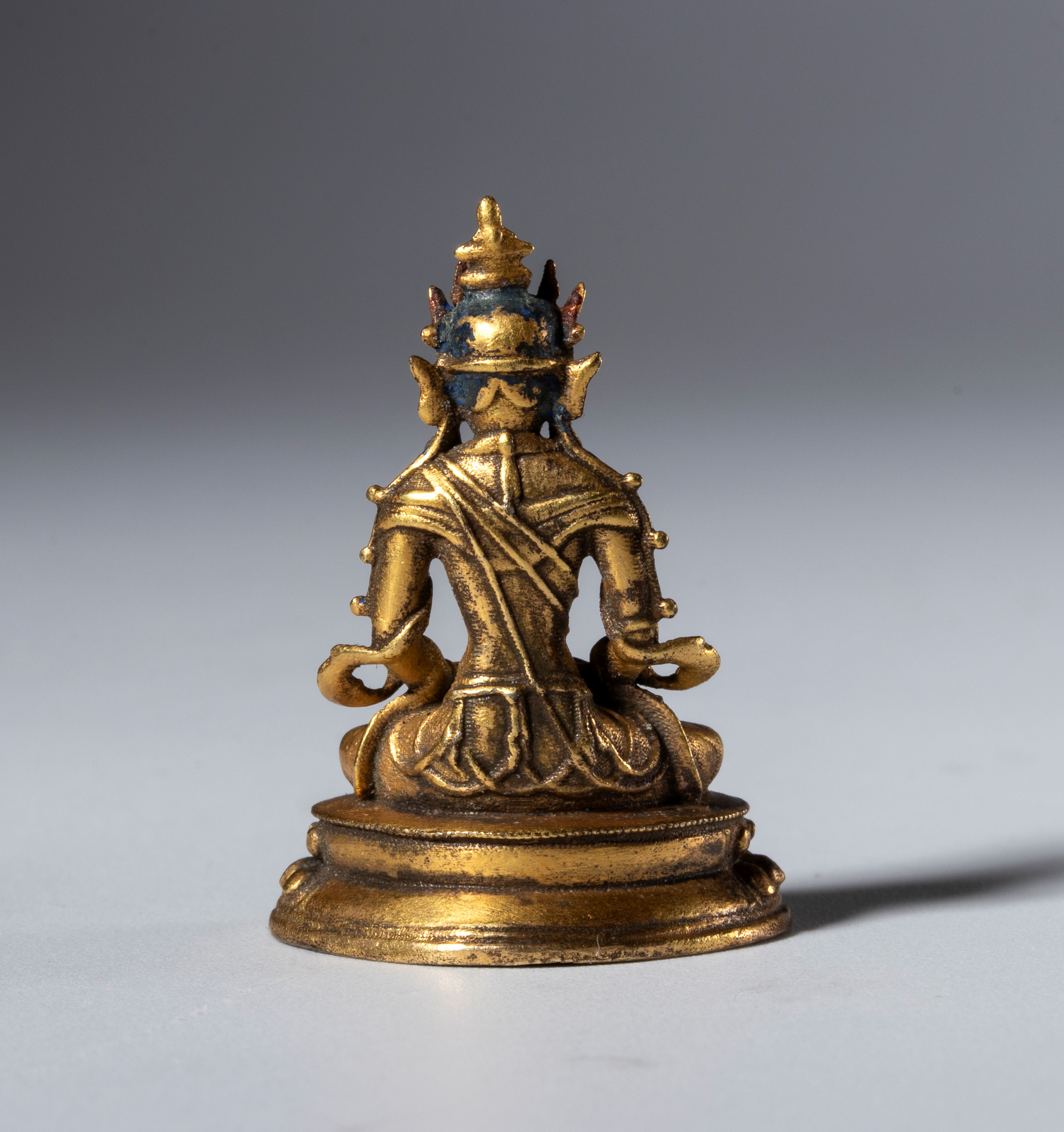Piccola statua di Buddha in rame dorato con base cava per reliquie. Tibet, XIX secolo