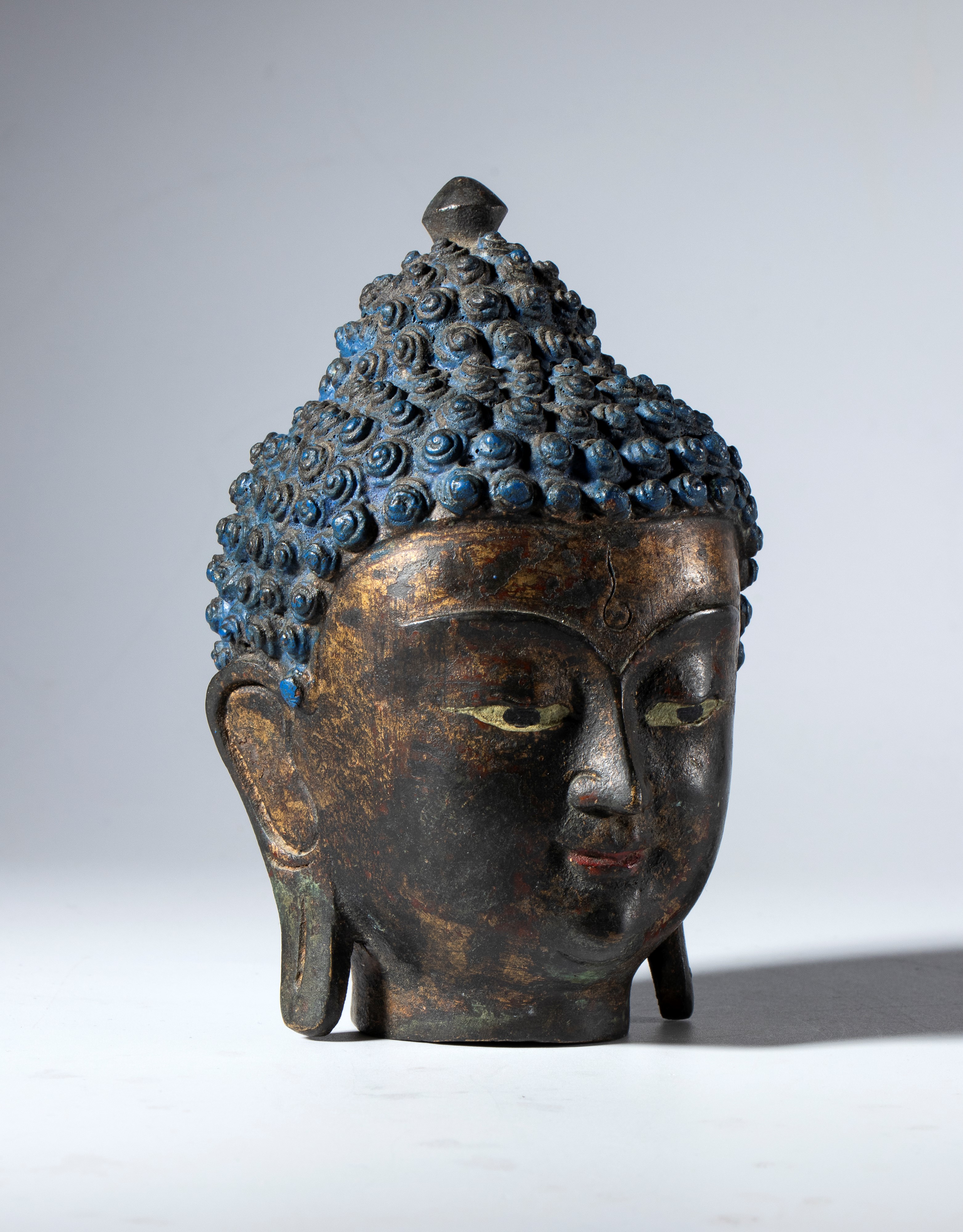 Testa di Buddha in lega di rame parzialmente dipinto. Area Himalayana, XIX secolo