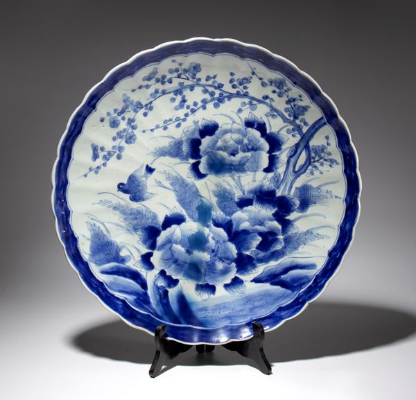 A large porcelain plate painted with blooming peonies, plum branches, and a small bird within a dark blue border. Japan, late 19th-20th century.