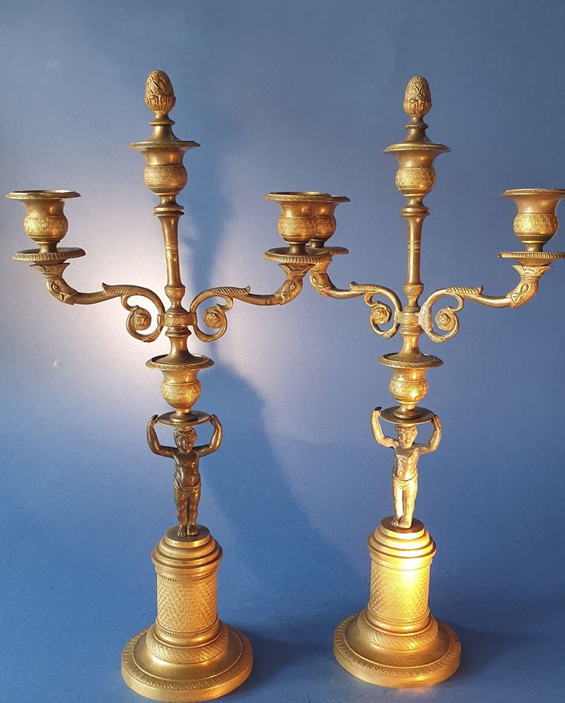 Coppia di candelieri con putti. Bronzo dorato e patinato nero. Primo XIX secolo.