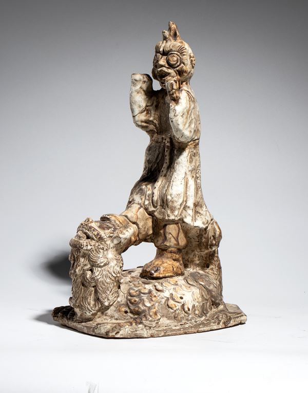 A white-glazed ceramic demon figure in traditional dress and a terrifying expression, resting on a mythological creature. Southeast Asia, 19th century.