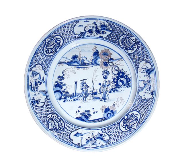 Grande piatto di produzione europea, in porcellana bianca e blu decorato con scene figurative orientaleggianti, bordo a motivi geometrici, floreali e paesaggistici. Europa, XVIII secolo