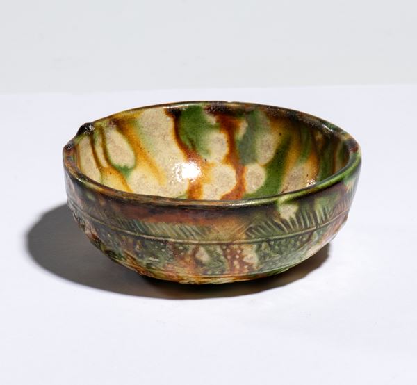A round ceramic bowl with sancai glaze and decorative reliefs on the exterior. China, Tang Dynasty, 8th century.