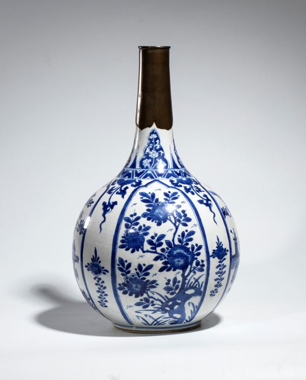 A blue and white porcelain bottle vase decorated with classical Chinese objects and floral motifs within a metal neck. China, Qing Dynasty, Kangxi Period. 